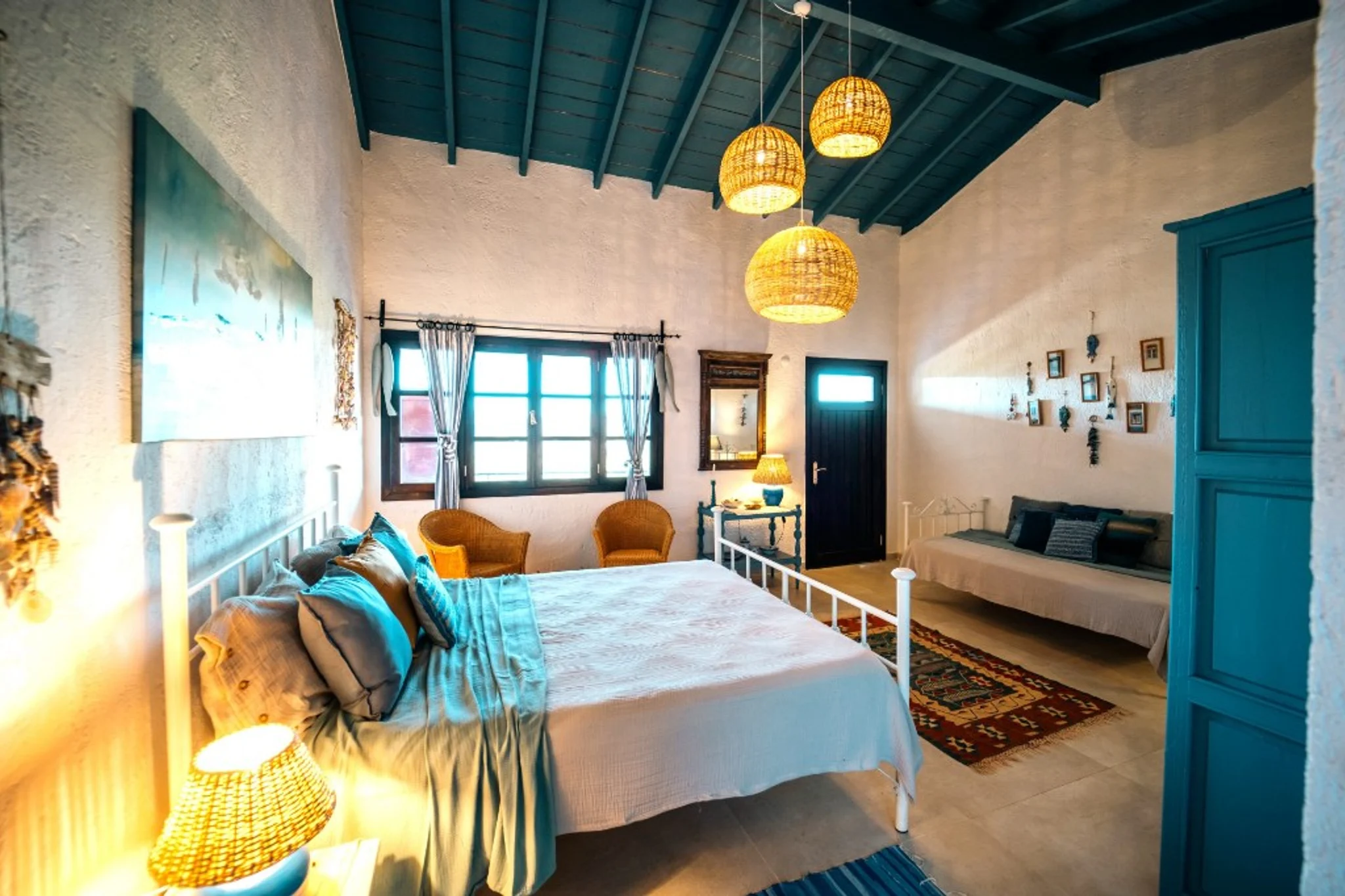 A guest room at dusk at Chef’s Atolye, with a teal beamed ceiling, woven lamps and a white iron bed